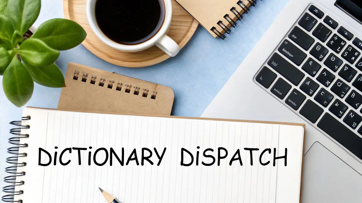 Overhead shot of a desk with a notebook showing 'DICTIONARY DISPATCH', a coffee cup, plant, and laptop.